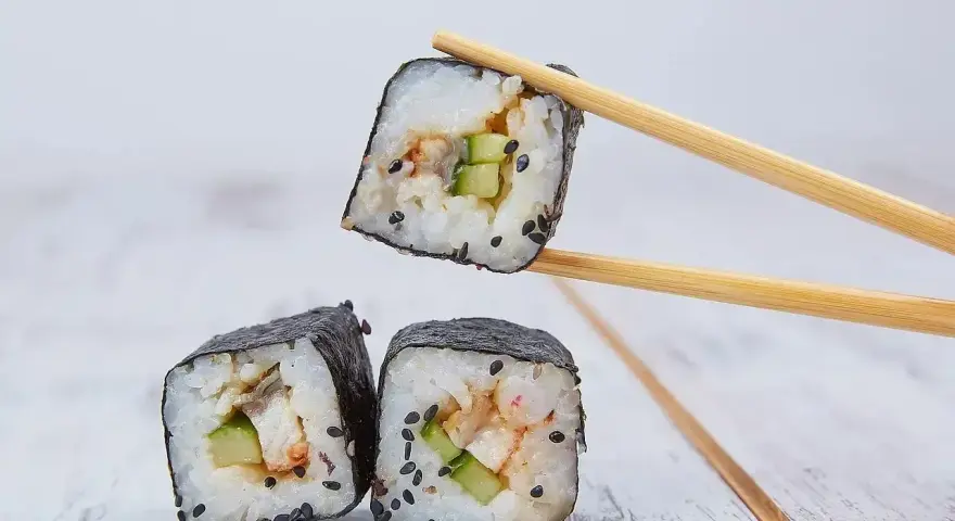 Rolka sushi z ogórkiem i rybą, podniesiona pałeczkami. Zastanawiasz się, ile octu ryżowego na 500g ryżu?