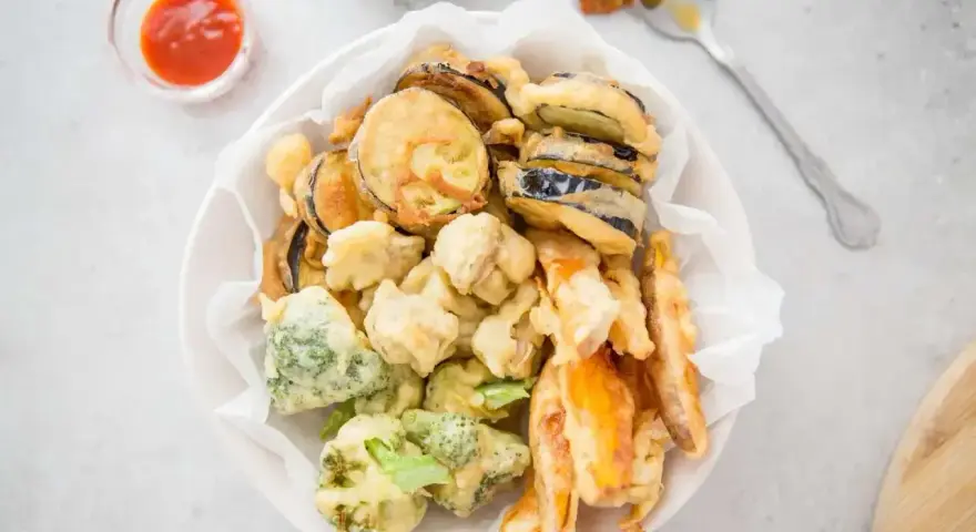 Chrupiące warzywa w cieście tempura: bakłażan, brokuły i marchewka, podane z sosem.