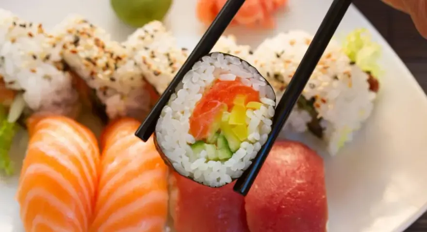 Pyszna rolka sushi z łososiem, ogórkiem i papryką, trzymana pałeczkami. Zastanawiasz się, ile waży rolka sushi?