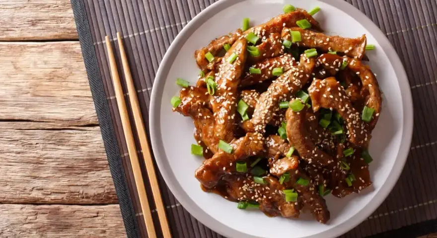 Pyszne kawałki wołowiny w sosie teriyaki, posypane sezamem i szczypiorkiem, gotowe do podania z pałeczkami.
