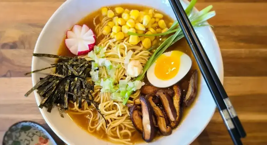 A miska pełna aromatycznego ramen miso z makaronem, jajkiem na pół, kukurydzą, grzybami shiitake, nori i szczypiorkiem.