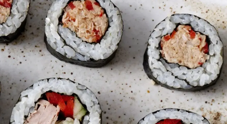 Kilka kawałków sushi z tuńczykiem i warzywami na talerzu.
