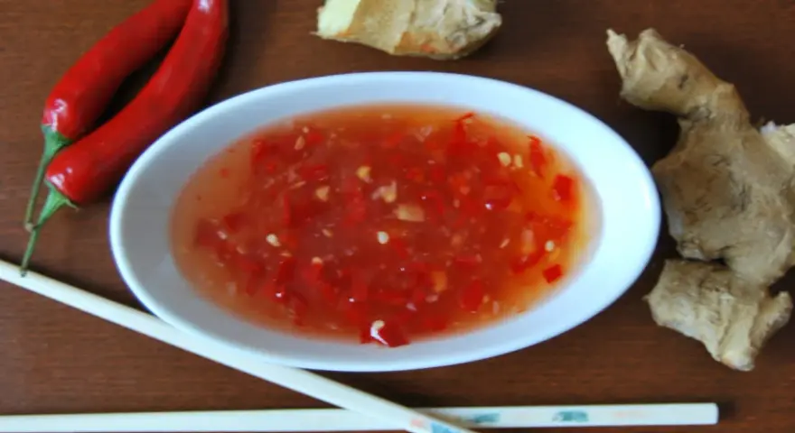Ostry sos tao tao z kawałkami chili i imbirem, obok pałeczki i papryczki.