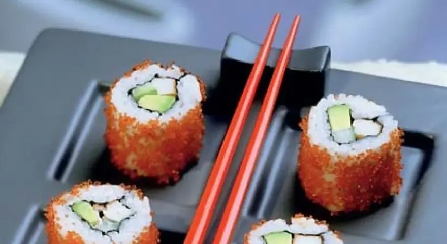 Cztery rolki sushi z awokado i rybą, obtoczone pomarańczową ikrą. Idealne sushi na diecie, podane z czerwonymi pałeczkami.