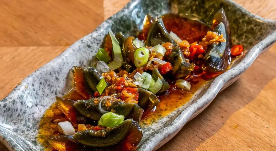 Kawałki 100 letniego jajka w pikantnym sosie z czosnkiem, chili i szczypiorkiem na kamiennej tacy.