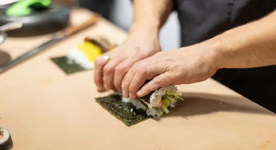 Dłonie zwijają sushi na arkuszu nori, ukazując jego wszechstronne właściwości kulinarne.