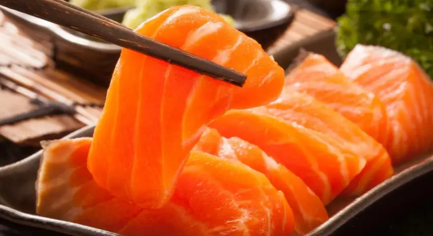 Sashimi co to? Świeży łosoś, chwytany pałeczkami, podany z wasabi i natką pietruszki.