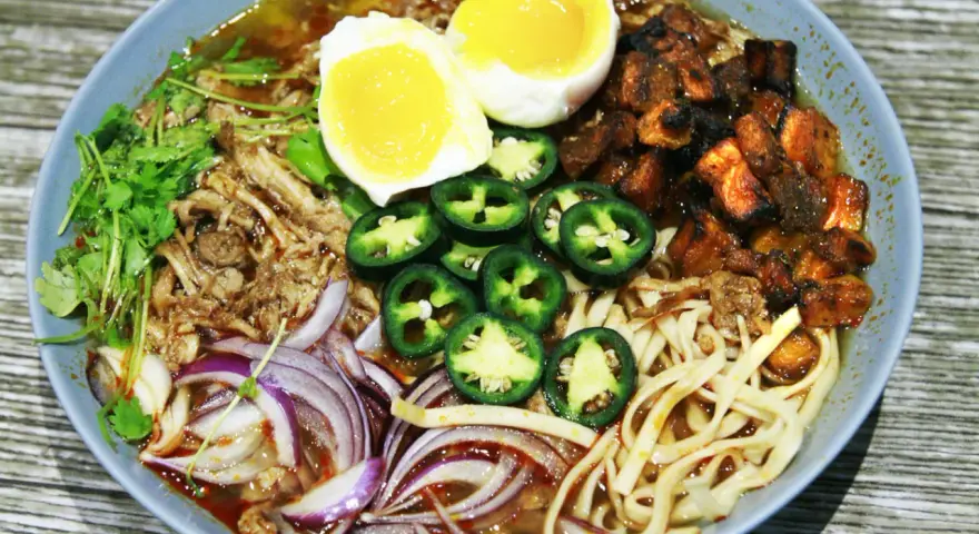 A miseczce ramen z wieprzowiną, jajkiem na pół, papryczkami jalapeño, cebulą i kolendrą.