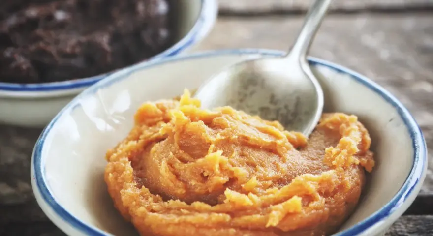 Pomarańczowa pasta miso w miseczce, obok ciemniejsza pasta. Łyżeczka zanurzona w jasnej paście.