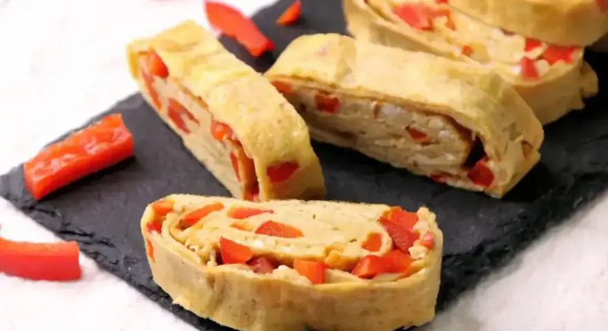 Roladki z jajek z papryką, przypominające omlet do sushi, ułożone na czarnej desce.