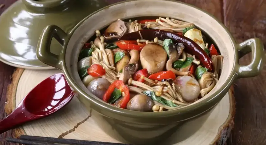 Gęsta zupa z grzybkami mun, enoki, pieczarkami, papryczkami chili i cebulką, podana w glinianym garnku.