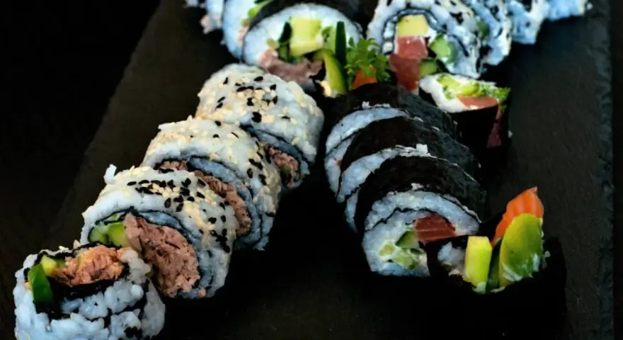 Pyszne rolki sushi z tuńczykiem i awokado, posypane sezamem. Idealna rzepa do sushi na czarnej desce.