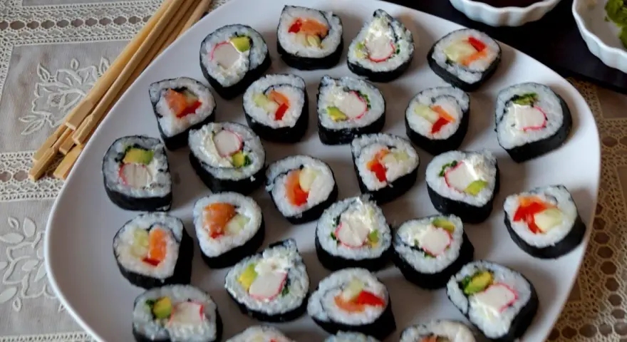 Talerz pełen sushi, w tym futomaki tamago z łososiem, awokado i paluszkami krabowymi.
