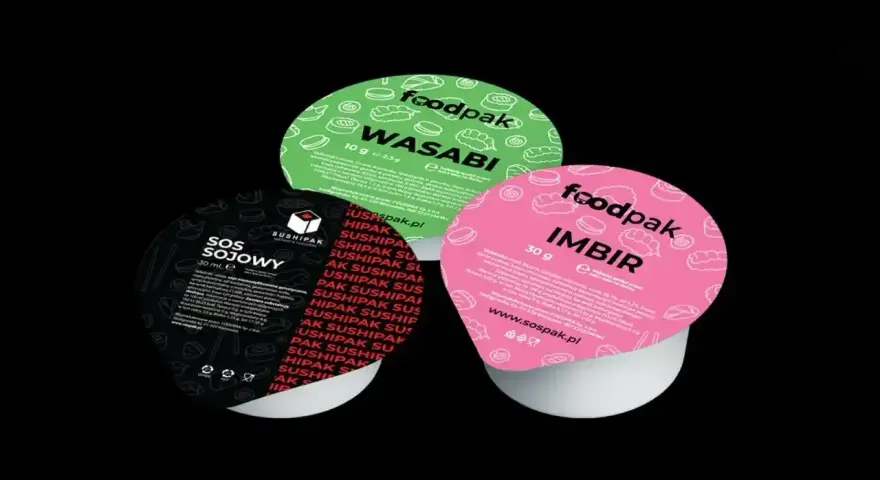 Trzy małe pojemniki z dodatkami do sushi: zielony z wasabi, różowy z imbirem i czarny z sosem sojowym.