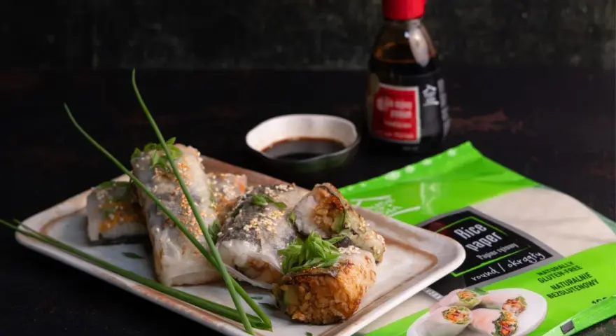 Pyszne sushi w papierze ryżowym, posypane sezamem, podane z sosem sojowym. Obok opakowanie papieru ryżowego.