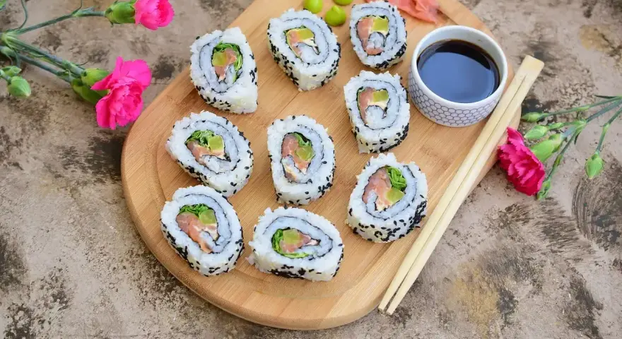 Pyszne california sushi z łososiem i awokado, posypane czarnym sezamem, podane z sosem sojowym i wasabi.
