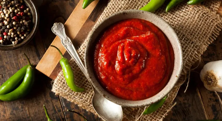 Miseczka z ostrym, czerwonym sosem, otoczona papryczkami chili, czosnkiem i pieprzem. Sriracha co to? To właśnie ten pikantny dodatek!
