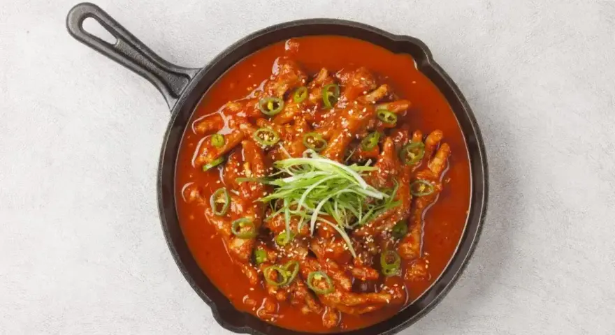 Kurczak w sosie gochujang, z zieloną cebulką i sezamem, podany na patelni.