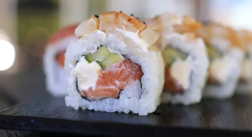 Uranaki z łososiem, kremowym serkiem i ogórkiem, zwieńczone krewetką. Pyszne danie sushi.