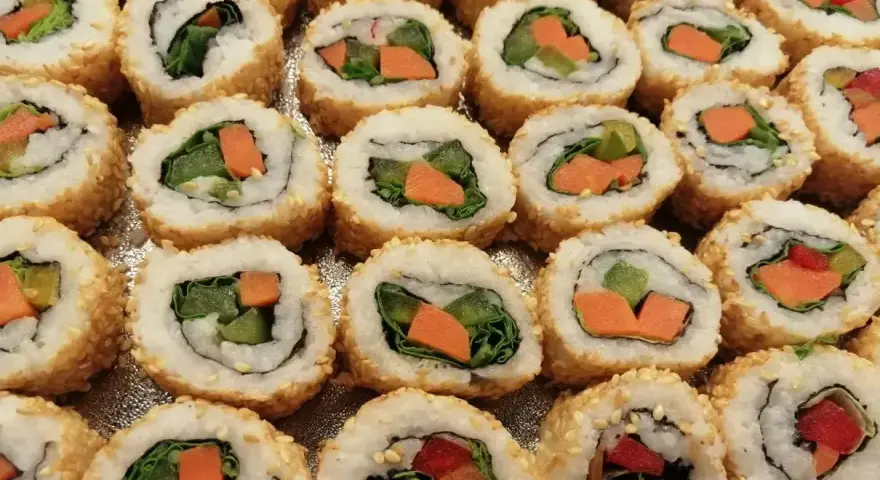 Roladki sushi z sezamem, w środku zielona sałata i pomarańczowa marchewka do sushi.