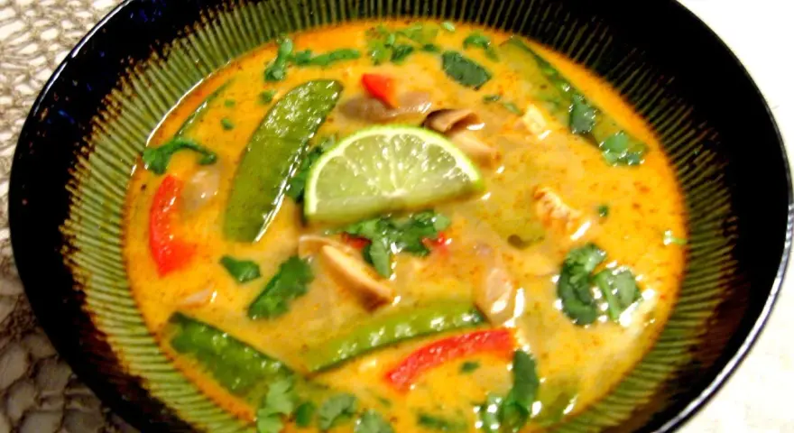 Aksamitna zupa tom kha z kurczakiem, z zielonym groszkiem, papryką i plasterkiem limonki.