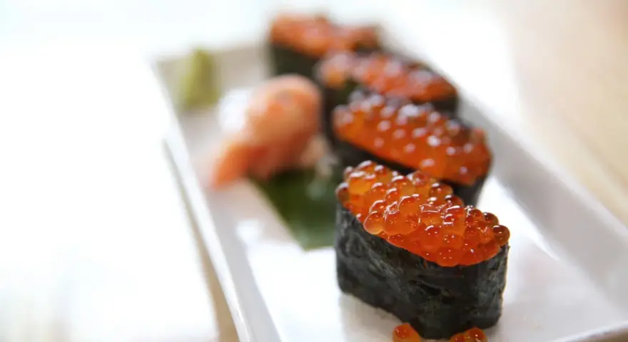 Pięć kawałków sushi z kawiorem, podanych na białym talerzu z odrobiną wasabi i marynowanego imbiru.