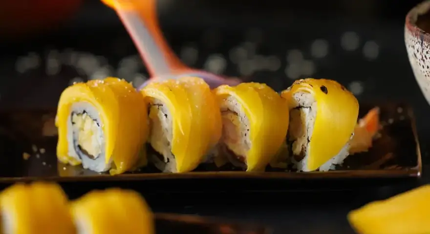 Płomień palnika opala sushi z mango, tworząc apetyczny wygląd.