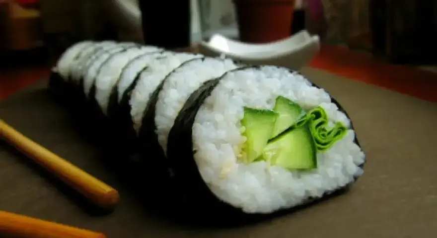 Świeży ogórek do sushi, zwinięty w rolkę z ryżem i nori. Obok leżą pałeczki.