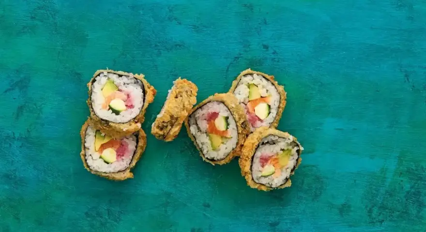Chrupiące sushi w panierce z łososiem, awokado i ogórkiem na turkusowym tle.