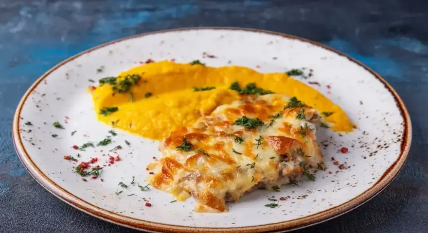 Pyszny katsu z kurczaka zapieczony z serem, podany z purée z dyni i posypany ziołami.