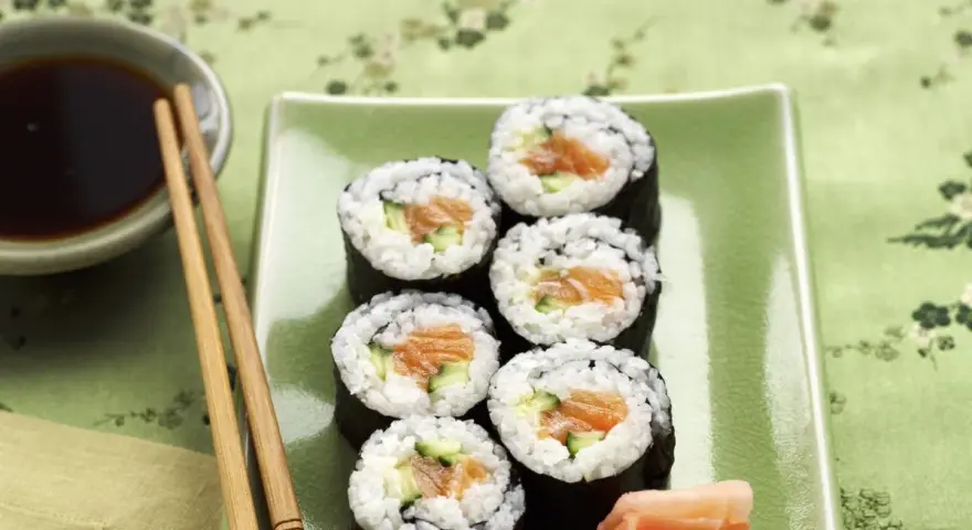 Sześć kawałków sushi z łososiem i ogórkiem, podanych z imbirem i sosem sojowym.