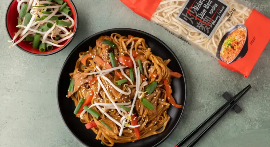 Pyszny makaron po azjatycku z kurczakiem, papryką i kiełkami fasoli mung. Obok opakowanie makaronu Chow Mein.