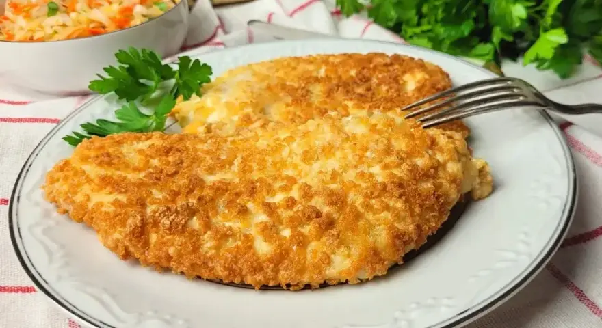 Dwa chrupiące kotlety z kurczaka w panko, podane na talerzu z sałatką z kapusty i marchewki.