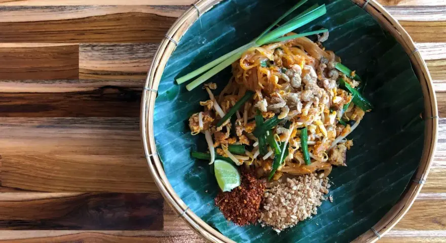 Pyszne pad thai skladniki: makaron ryżowy, kiełki, szczypiorek, orzeszki ziemne, chili i limonka na liściu bananowca.