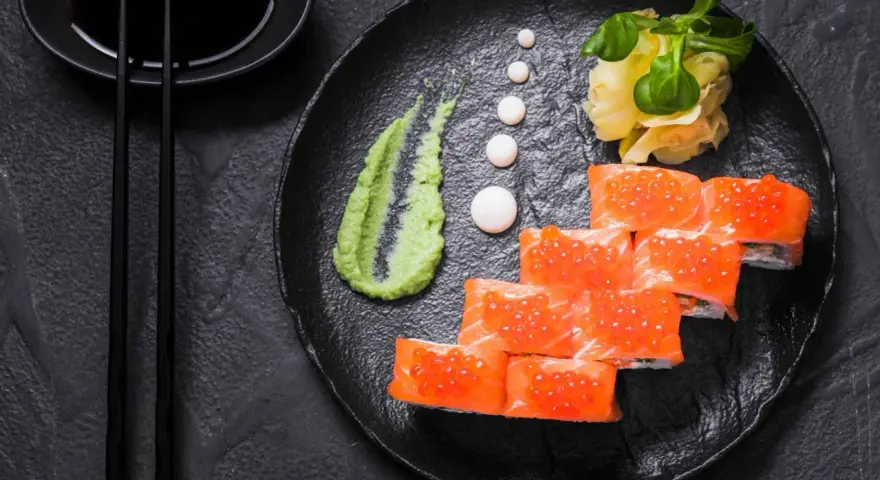 Roladki sushi z łososiem i ikrą, podane z zielonym, pikantnym wasabi prawdziwe, imbirem i sosem sojowym.