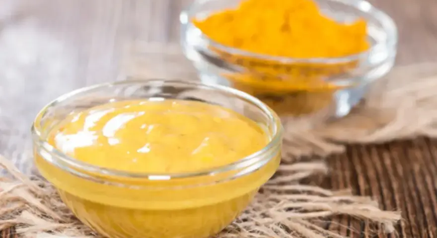 Dwie szklane miseczki na drewnianym tle. Jedna zawiera gładki sos, druga żółtą przyprawę, składniki do korma curry.