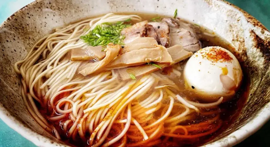 Miseczka aromatycznego ramenu z makaronem, jajkiem, mięsem i bambusem. Widać wyraźnie dodane ramen przyprawy, które nadają daniu głębi smaku.