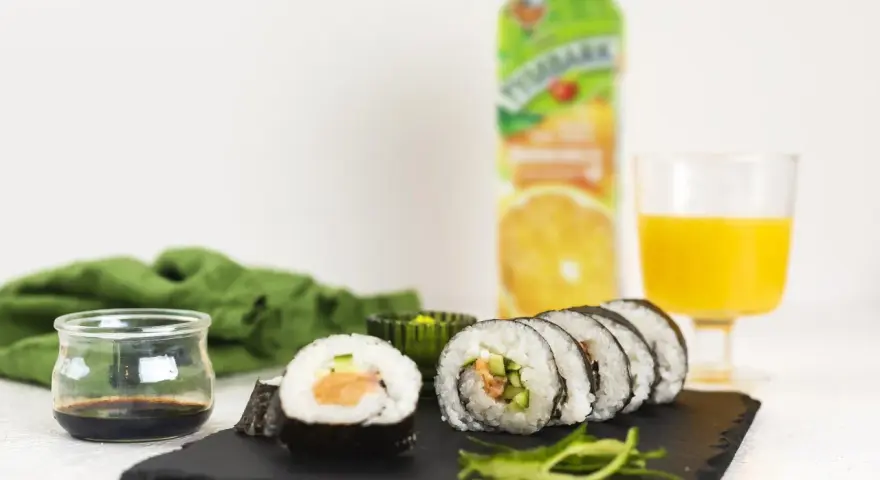 Roladki sushi z surowym łososiem do sushi, ogórkiem i ryżem, podane z sosem sojowym i sokiem pomarańczowym.
