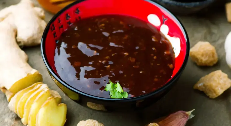 Sos teriyaki przepis: miseczka z ciemnym sosem, obok imbir, czosnek, cukier trzcinowy i miód. Idealny do dań azjatyckich.