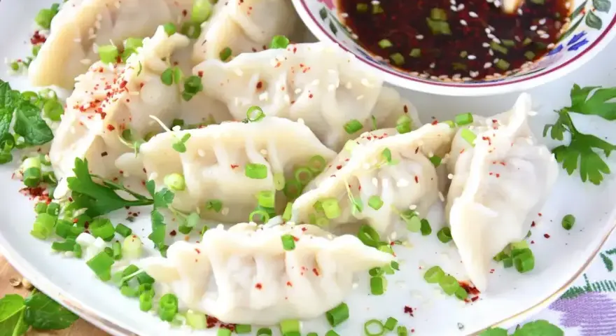 Pyszne pierożki gyoza posypane szczypiorkiem i sezamem, podane z aromatycznym sosem.