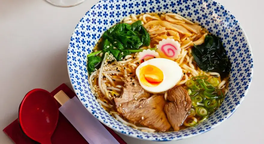 Miseczka aromatycznego makaronu ramen z jajkiem, mięsem, warzywami i kiełkami. Idealny posiłek, który dostarczy energii i zaspokoi głód.