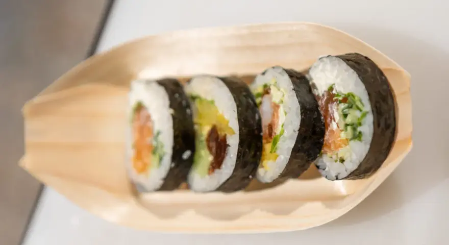 Pięć kawałków sushi z łososiem, awokado i krewetkami na drewnianej łódce. Różne rodzaje sushi nazwy.