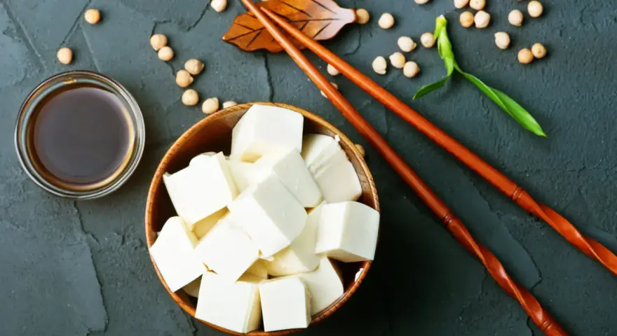 Kostki tofu, czyli przetworzona fasola sojowa, w drewnianej misce, obok sosu sojowego i pałeczek.