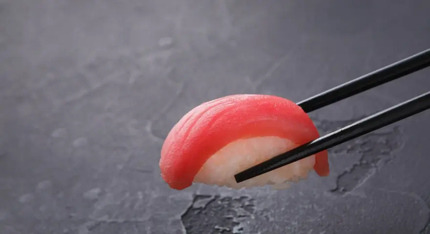 Pałeczki trzymają kawałek sushi z tuńczykiem. Czy sushi jest dobre? Wygląda apetycznie!