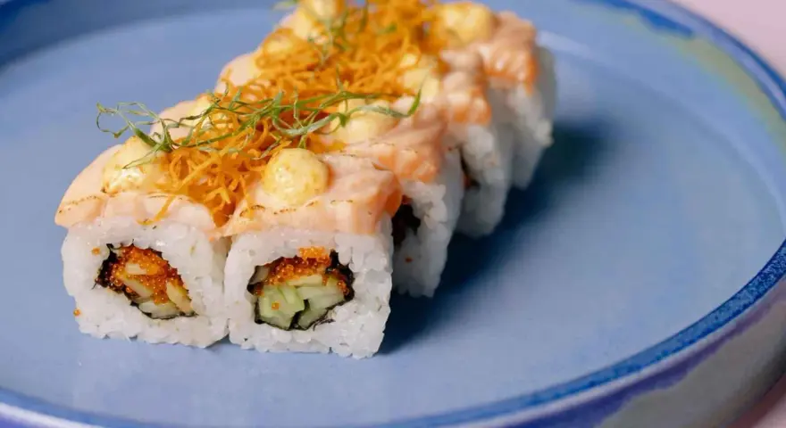 Roladki sushi z łososiem i chrupiącą posypką, z delikatnym akcentem, który przypominałby wasabi w ciąży, gdyby nie był to sos.