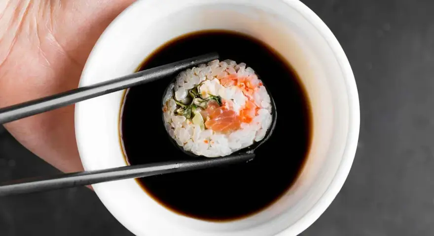Pałeczkami zanurzam sushi z łososiem i kremowym nadzieniem w sosie sojowym. Idealny sojowy ser do sushi.