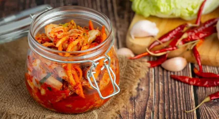 Słoik z kimchi na tle desek, z suszonymi papryczkami chili i czosnkiem.