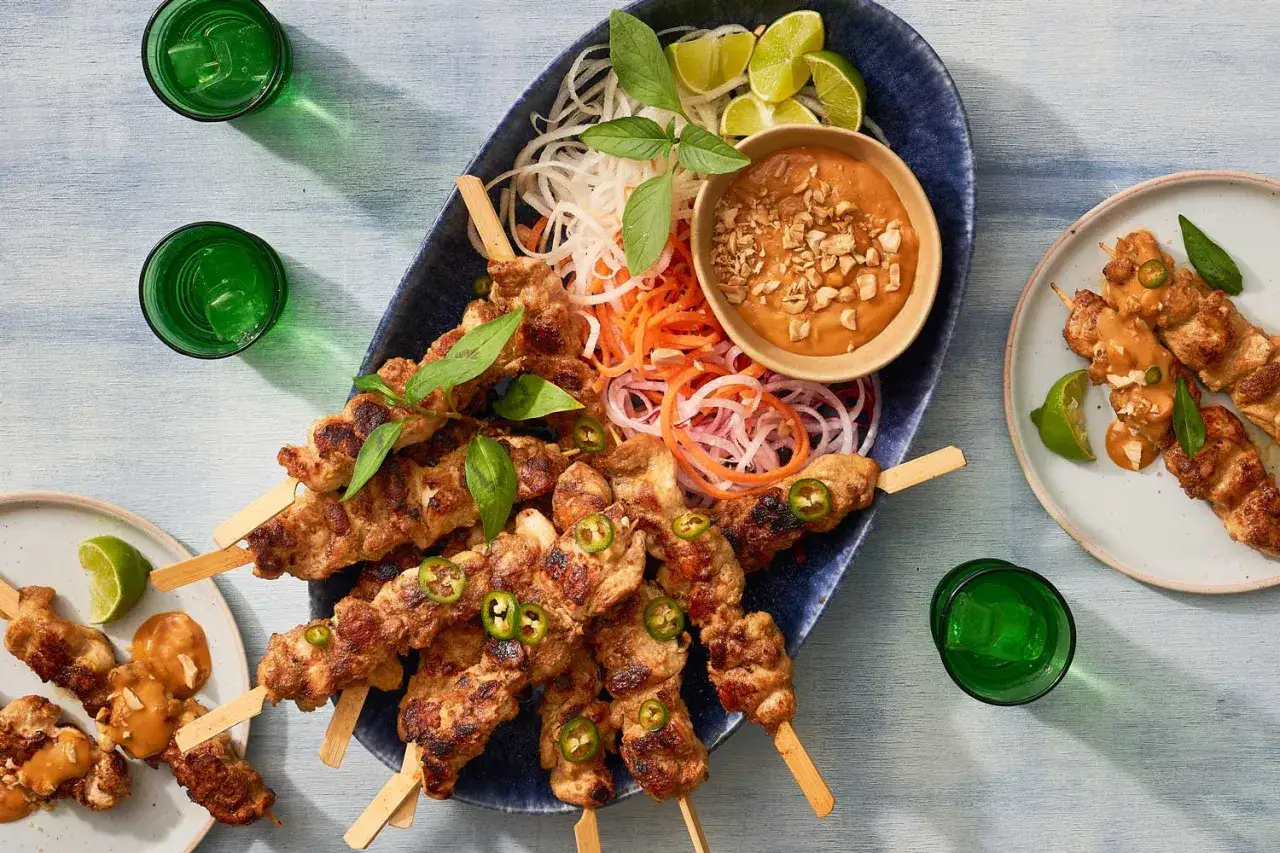 Pyszny satay z kurczaka na patyczkach, podany z orzechowym sosem, świeżymi warzywami i limonką. Idealna przekąska na lato.