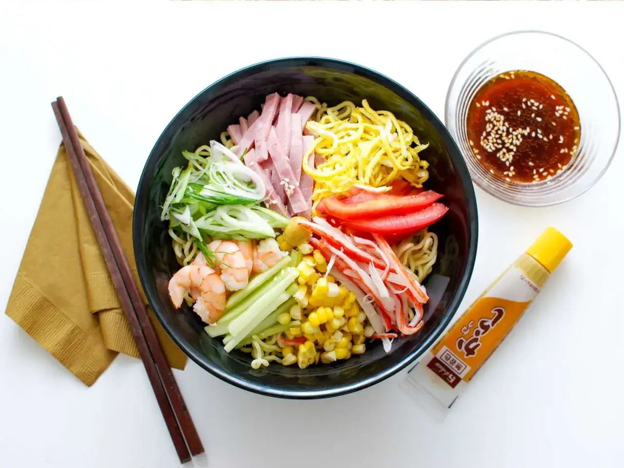 Kolorowe ramen z krewetkami, szynką, krabem, kukurydzą, pomidorem i jajkiem. Sos sezamowy obok.