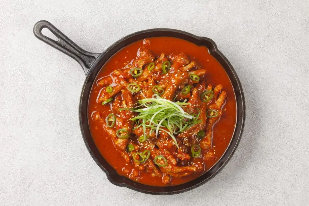 Kurczak w pikantnym sosie gochujang, podany w żeliwnej patelni, ozdobiony zieloną cebulką i sezamem.